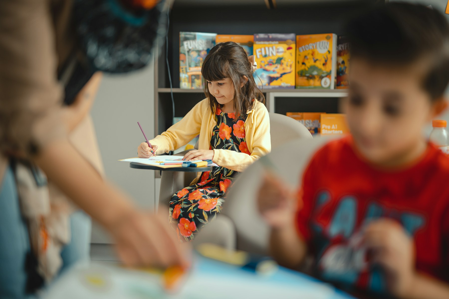 A student works at a classroom desk while classmates sit nearby.